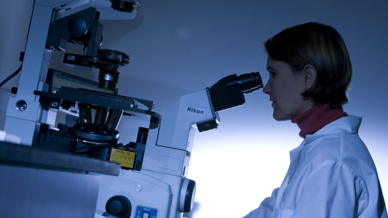 Woman looking into a microscope. Pane Image 1