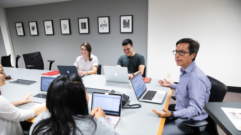 A professor at USC Annenberg teaches a small class with students around a table.