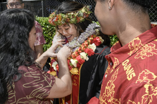 A graduating Trojan smiles as her parents place a garland over her head
