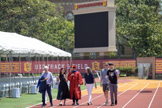 A graduating PhD student and family walk on the USC track