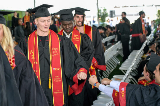 A USC graduate giving a fist bump to another student