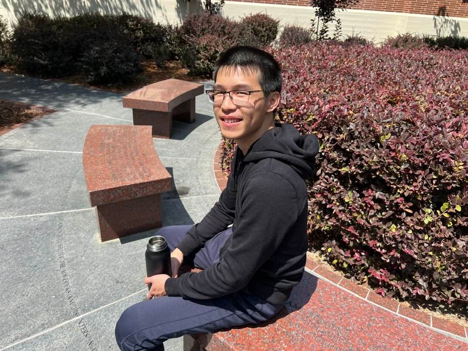 USC Viterbi student Jonathan Tam sits on a red marble bench, part of the Blacklist installation outside the USC Fisher Museum of Art. (Photo/Greg Hernandez)