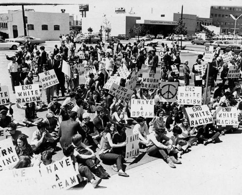 A large crowd of people standing or seated with signs reading “End White Racism,” “I Have a Dream” and “We Mourn Dr. King.”