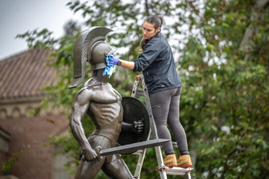 Conservator Meg Driscoll cleans Tommy Trojan in preparation for Commencement