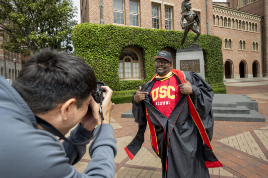 Rick Jones poses for a photograph with his USC alumni shirt under robes
