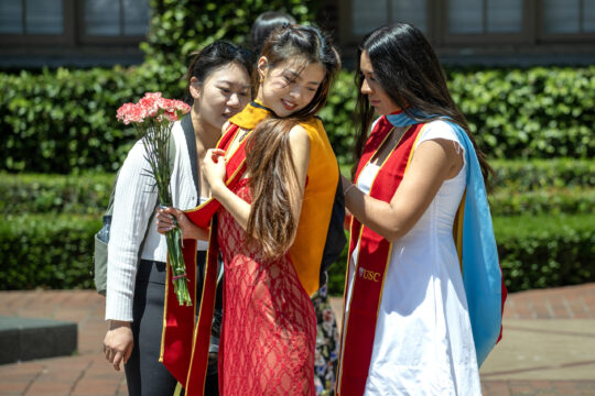 A fellow graduating student assist another with her sash