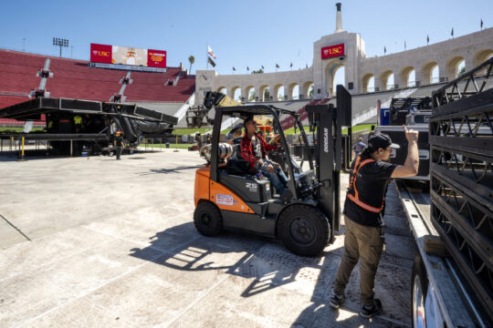 Crews work on setting up the historic Los Angeles Memorial Coliseum with a forklift for USC commencement
