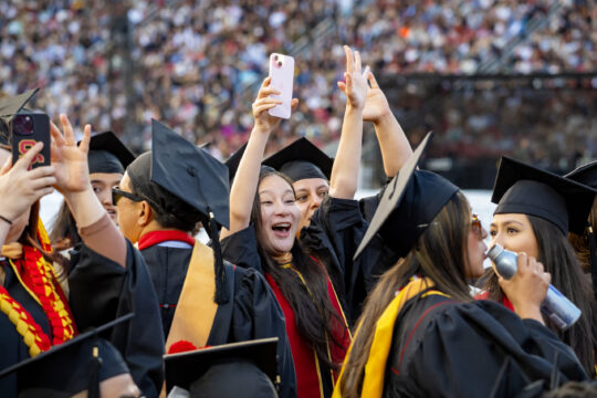 USC graduates smile with hands in the air