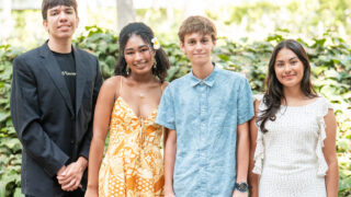 Four USC Bovard Scholars students stand together outdoors, smiling, with greenery in the background.